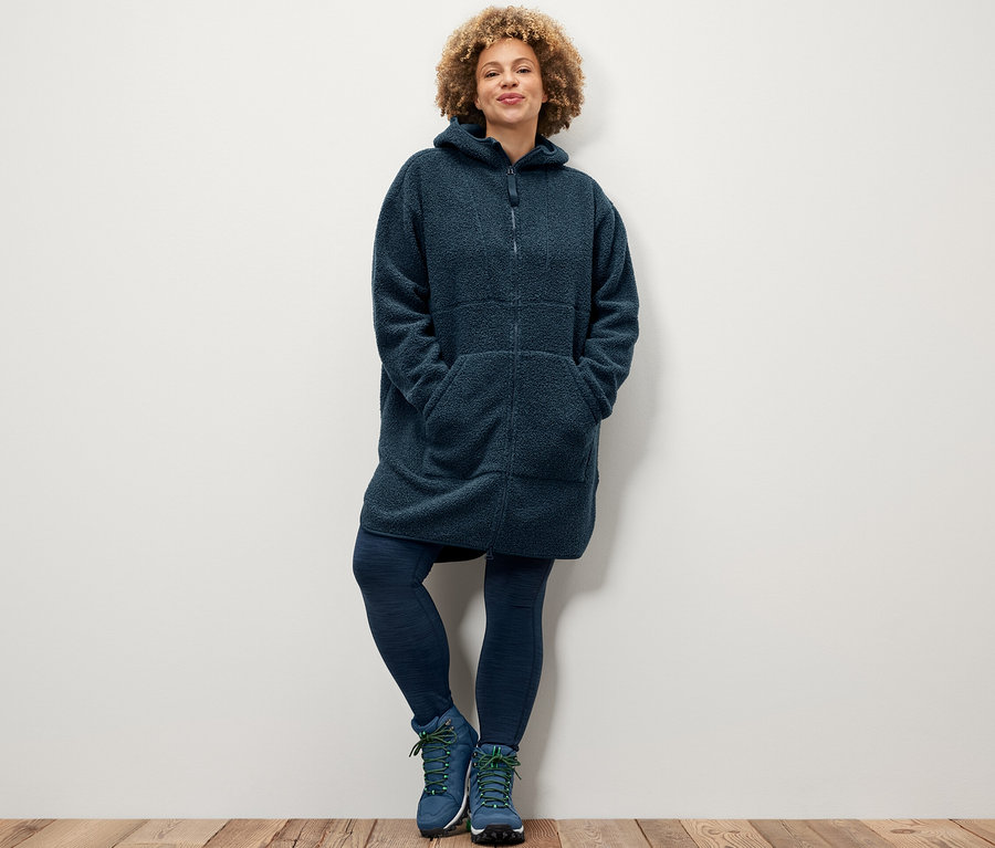 Frau posiert in Sporttights und einem oversized Teddy-Mantel.