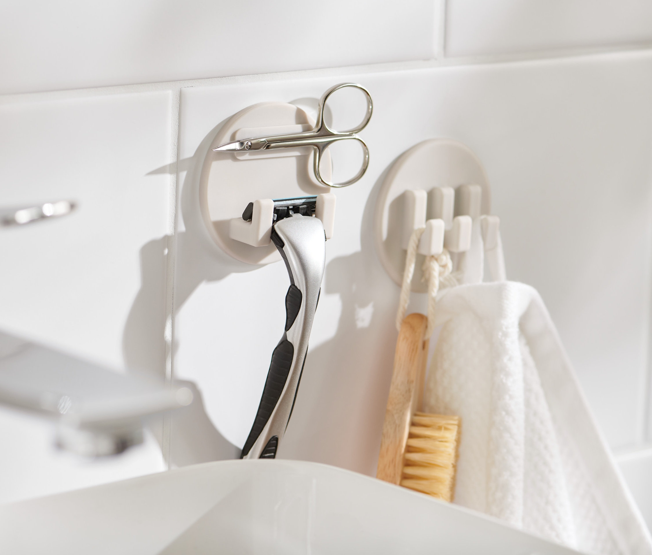 Zwei selbsthaftende Halter-Sets an weißen Fliesen, eines mit Rasierer und Schere.
