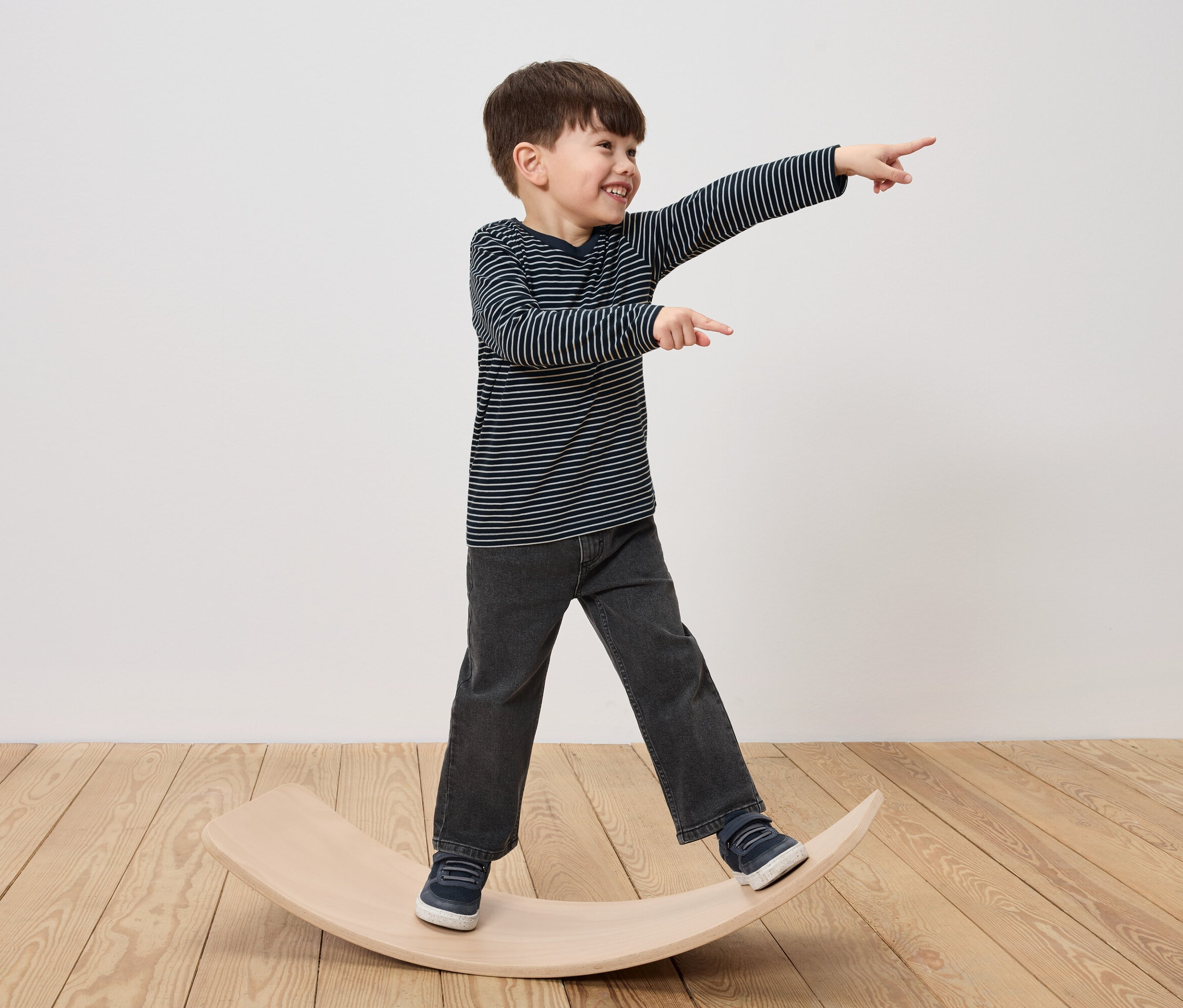 Ein Junge steht auf einem hölzernen Balance Board, lacht und zeigt mit dem Finger.