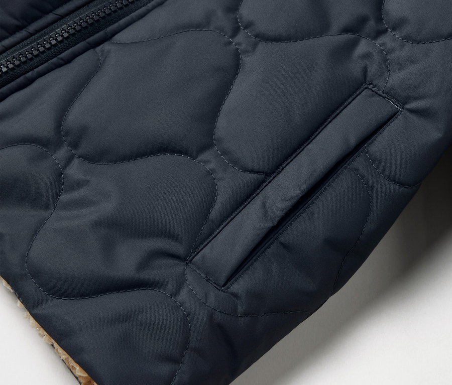 Detail einer gesteppten Kinder-Wendejacke mit Tasche und Reißverschluss.