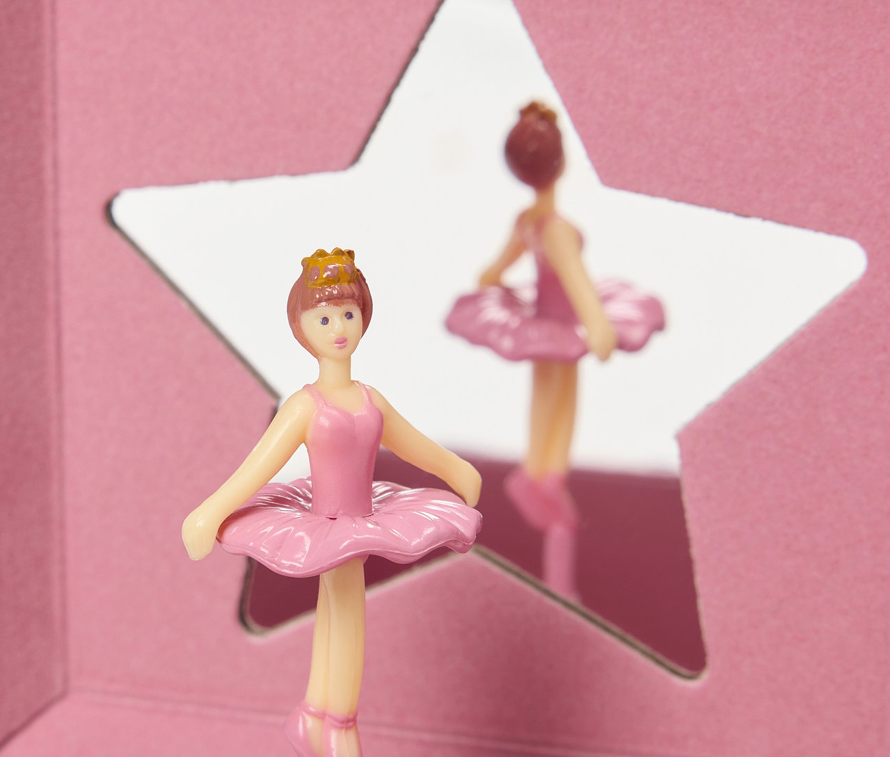 Eine rosa Ballerina-Figur mit Krone steht vor einem sternförmigen Spiegel.
