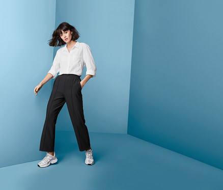 Frau posiert in einer schwarzen Funktionshose in Rippoptik, einer weißen Bluse und Turnschuhen.