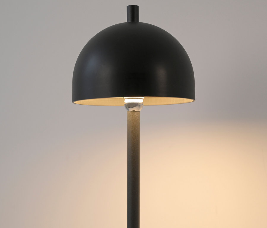 Eine schwarze Lampe mit rundem Schirm beleuchtet den Raum.