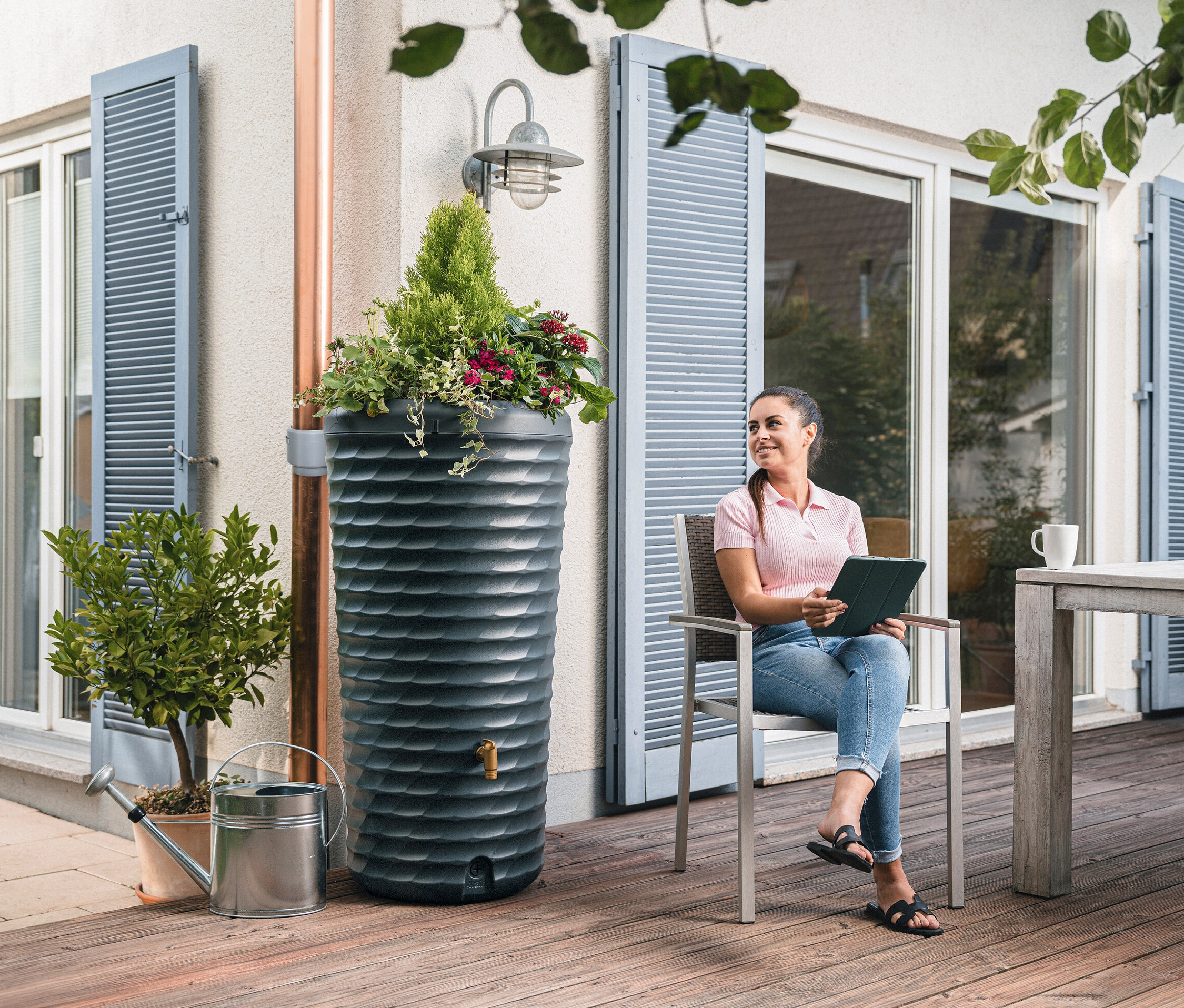 Frau sitzt neben Garantia 2-in-1-Regentonne-Komplett-Set, ca. 230 l und hält Tablet.