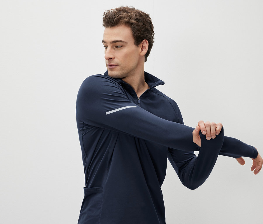Mann dehnt Arm in dunkelblauem Sport-Langarmshirt.