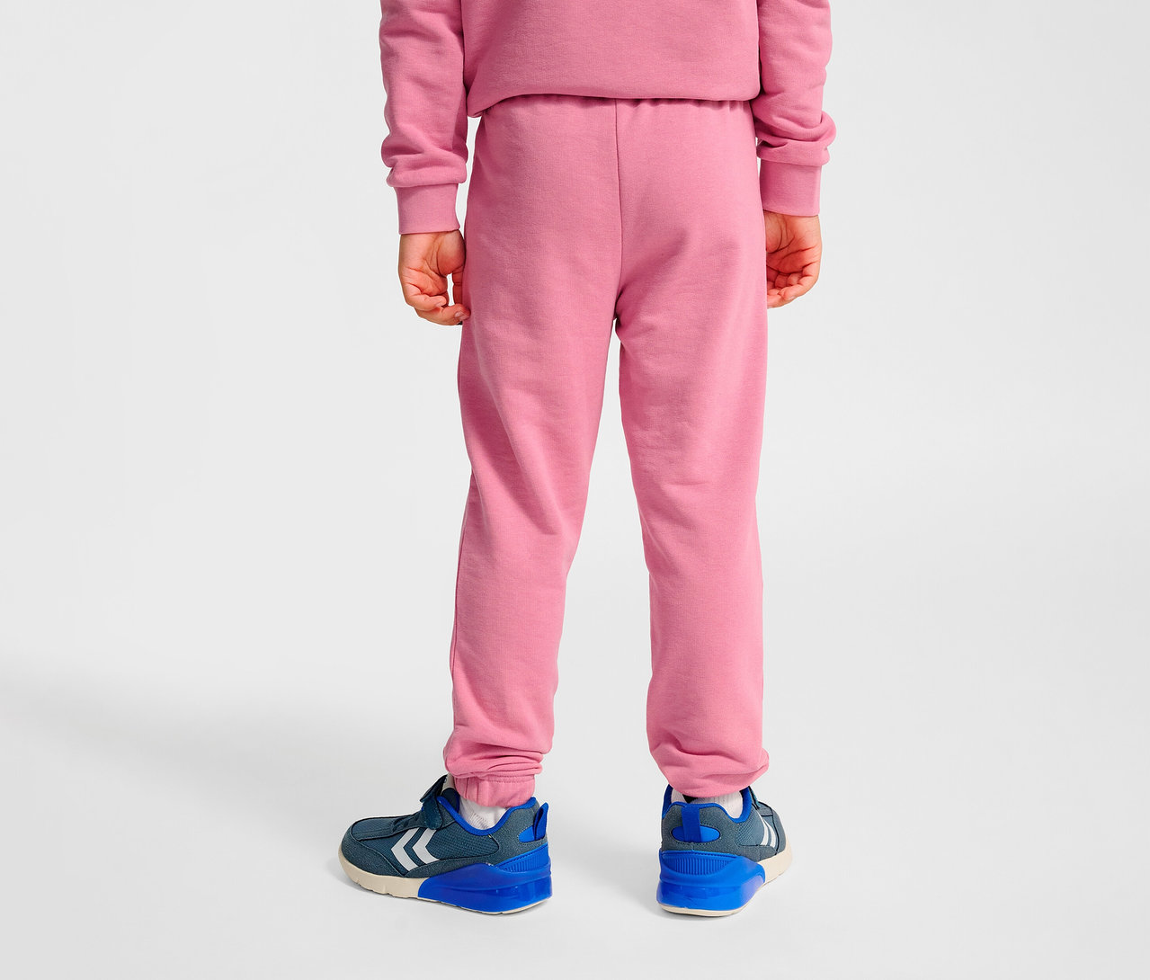Rückansicht eines Kindes, das rosa HUMMEL HMLJR Base Regular Pants und blaue Schuhe trägt.