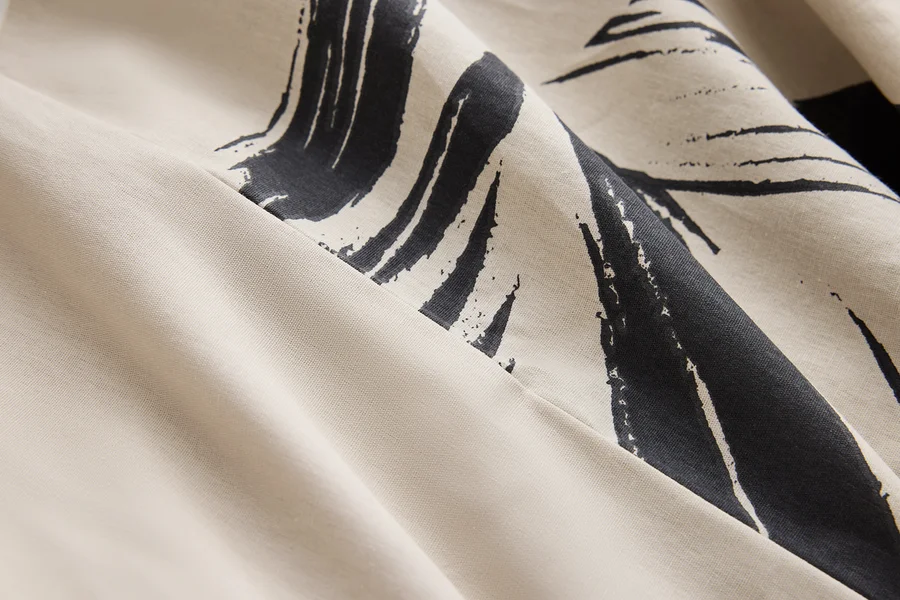 Detailaufnahme eines cremefarbenen Stoffes mit dunkelblauem abstraktem Muster.