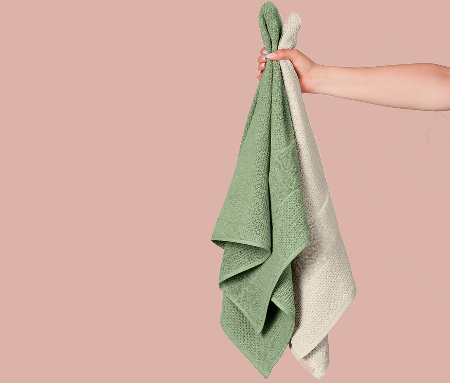 Eine Hand hält zwei Textilhantücher: ein grünes und ein cremefarbenes.
