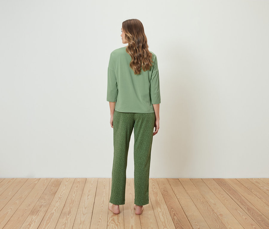 Frau steht mit dem Rücken zum Betrachter und trägt einen grünen Pyjama.