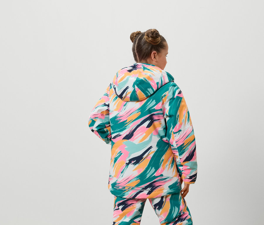 Von hinten ist ein Mädchen in einer bunten Jacke und Hose zu sehen.