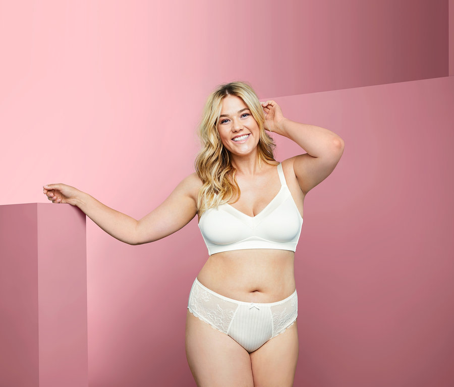 Frau posiert in Soft-BH und Unterhose vor pinkfarbenem Hintergrund.