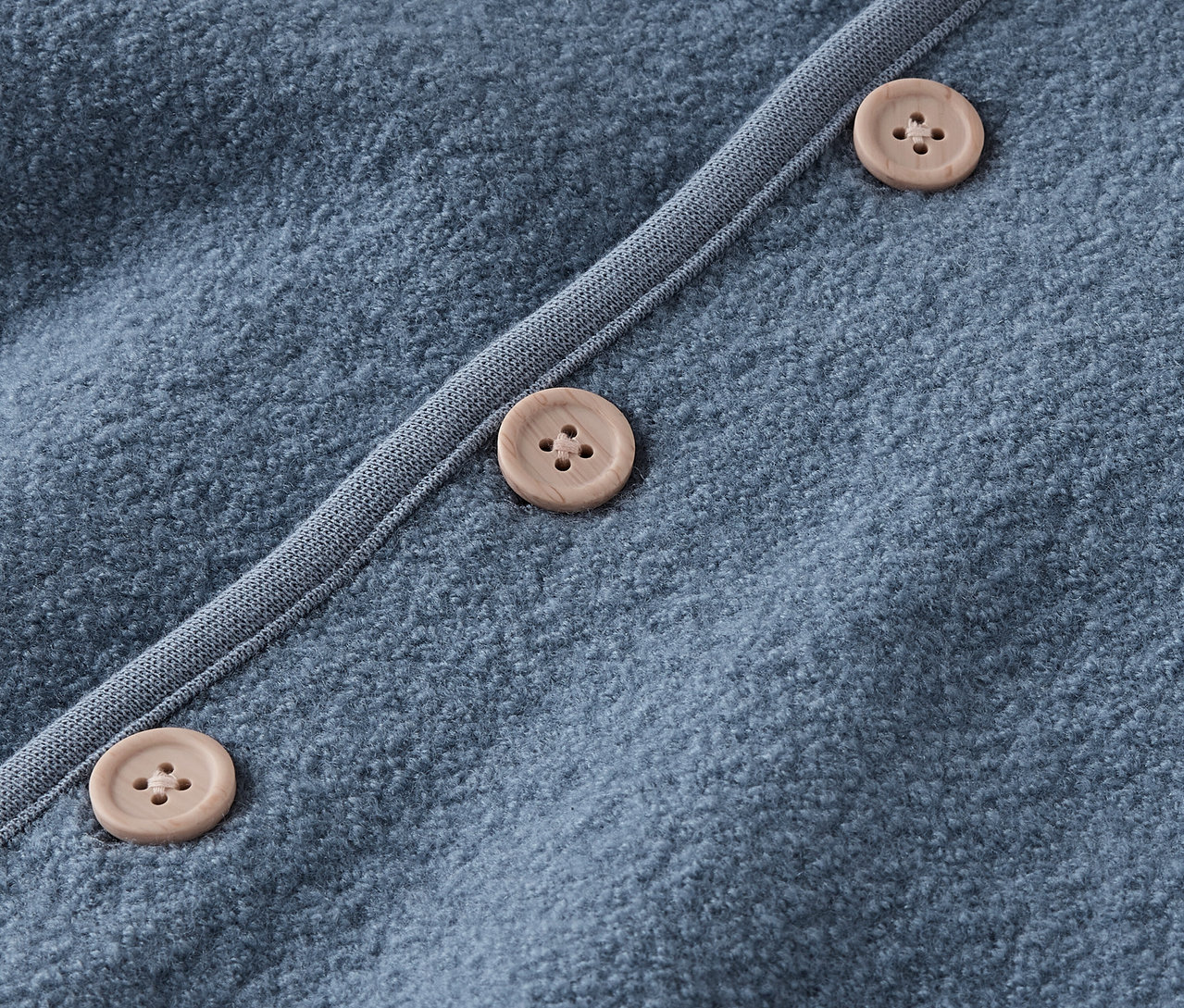 Detailaufnahme eines blauen Pullovers mit braunen Knöpfen.