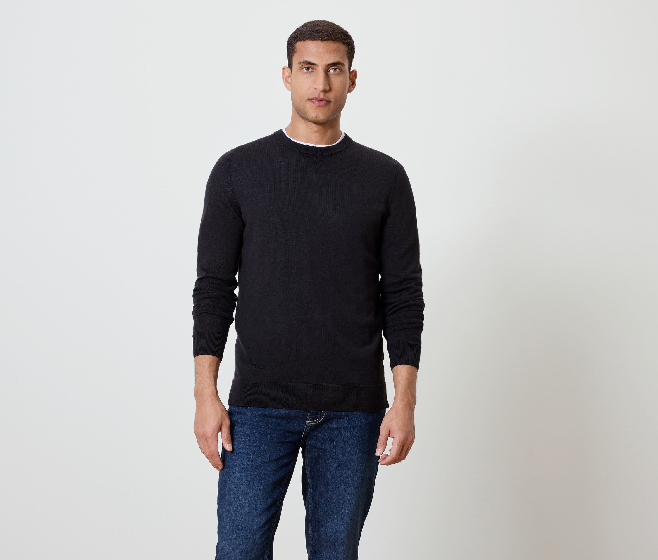 Ein Mann steht und trägt einen schwarzen Pullover und blaue Jeans.