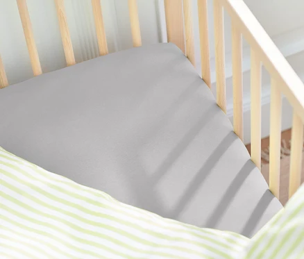 Detailaufnahme eines Kinderbetts mit grauem Spannbettlaken und einem Kissen mit grünen Streifen.