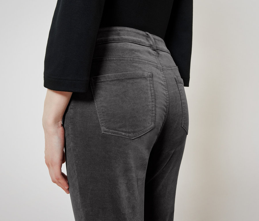 Rückansicht einer Frau mit schwarzem Oberteil und grauen Cordhosen.