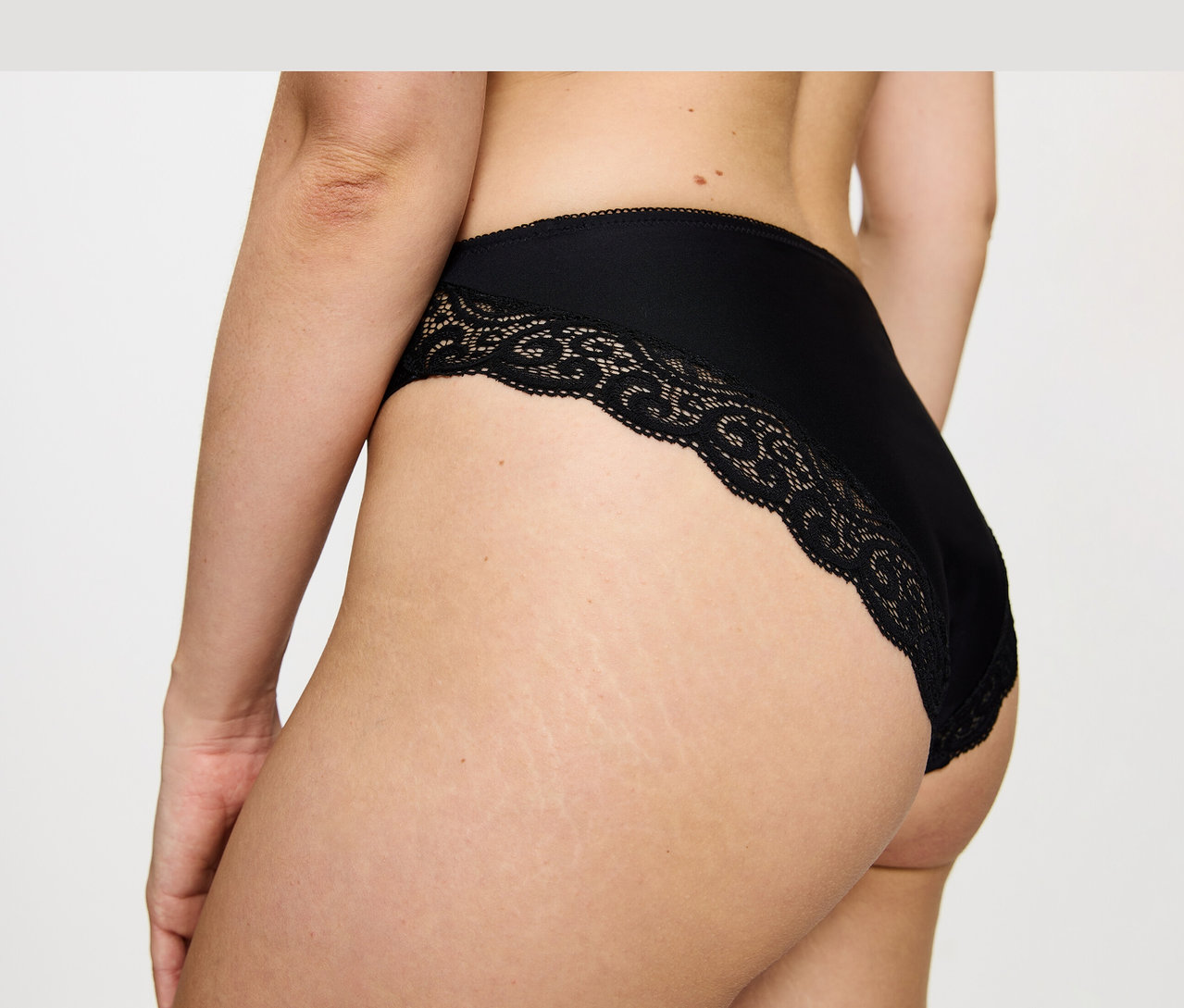 Nahaufnahme des Rückens einer Person, die einen schwarzen Triumph Amourette Tai Slip mit Spitzenbesatz trägt.