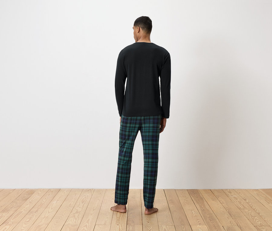 Mann von hinten trägt ein schwarzes Langarmshirt und eine grün karierte Pyjamahose.