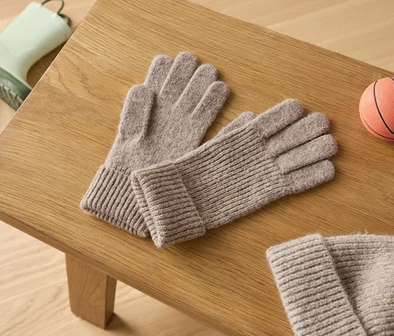 Auf einem Holztisch liegen ein Paar graue Strickhandschuhe, ein Paar grüne Gummistiefel und ein kleiner orangefarbener Basketball.