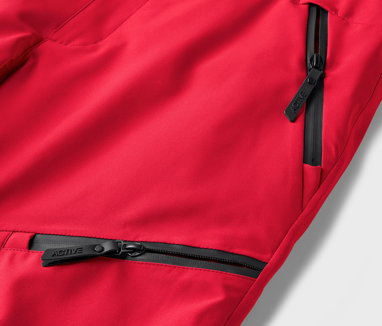 Detail einer roten Hose mit schwarzen Reißverschlüssen an den Taschen.