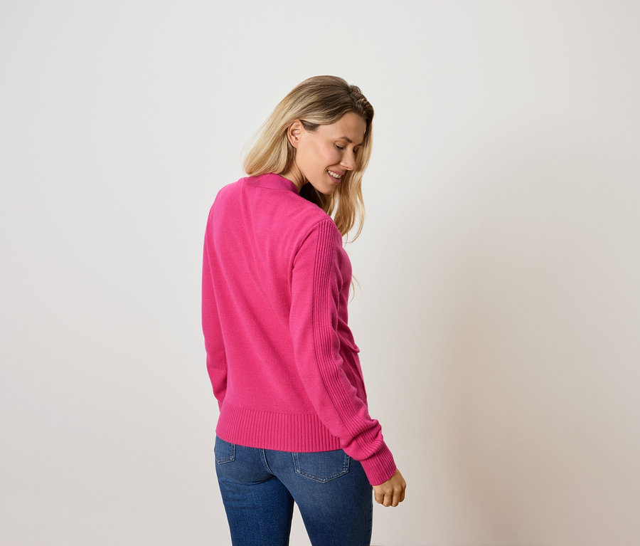 Frau schaut nach unten und trägt einen pinken Pullover und Jeans.