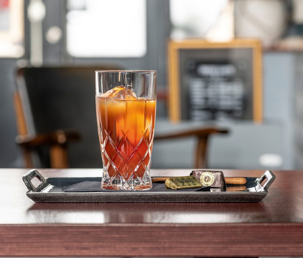 Ein Nachtmann Latte-Macchiato-Glas »Noblesse« gefüllt mit einem Getränk und Eiswürfeln steht auf einem Serviertablett.