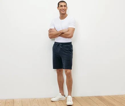 Mann steht mit verschränkten Armen und trägt blaue Frottee-Shorts.