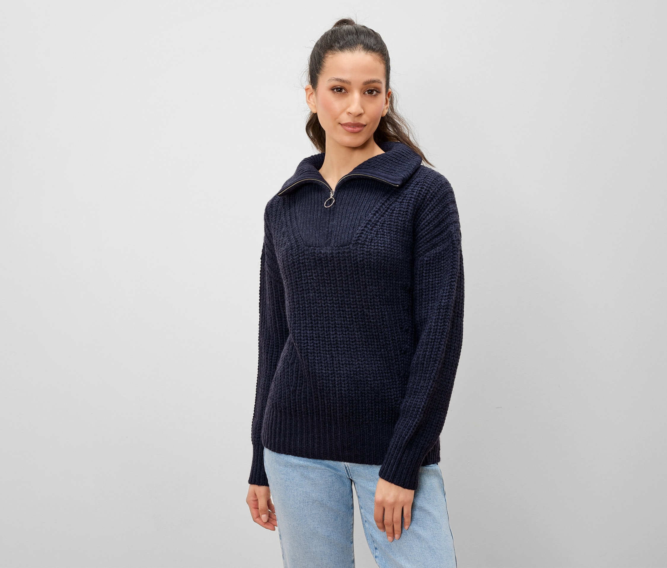 Frau posiert in marineblauem Strickpullover mit Reißverschluss und heller Jeans.