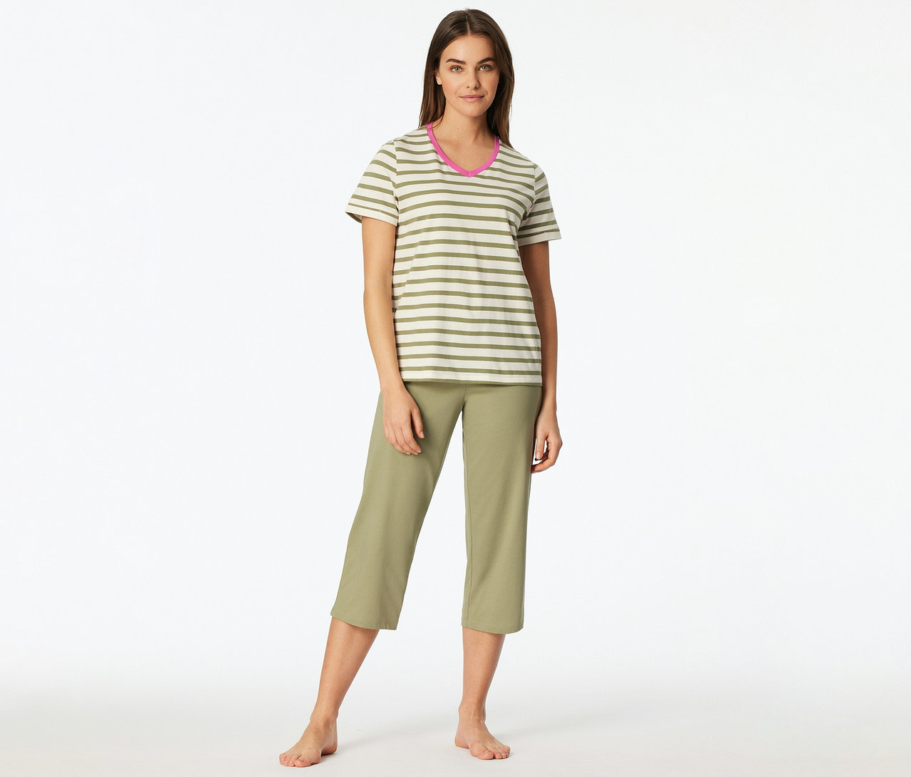 Eine Frau steht barfuß und trägt ein SCHIESSER 3/4-Pyjama-Set. Das Oberteil ist gestreift in Grün und Weiß mit pinkem V-Ausschnitt, die Hose ist eine grüne Caprihose.