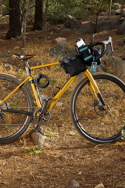 Gelbes Fahrrad mit schwarzen Taschen und Zubehör im Wald.