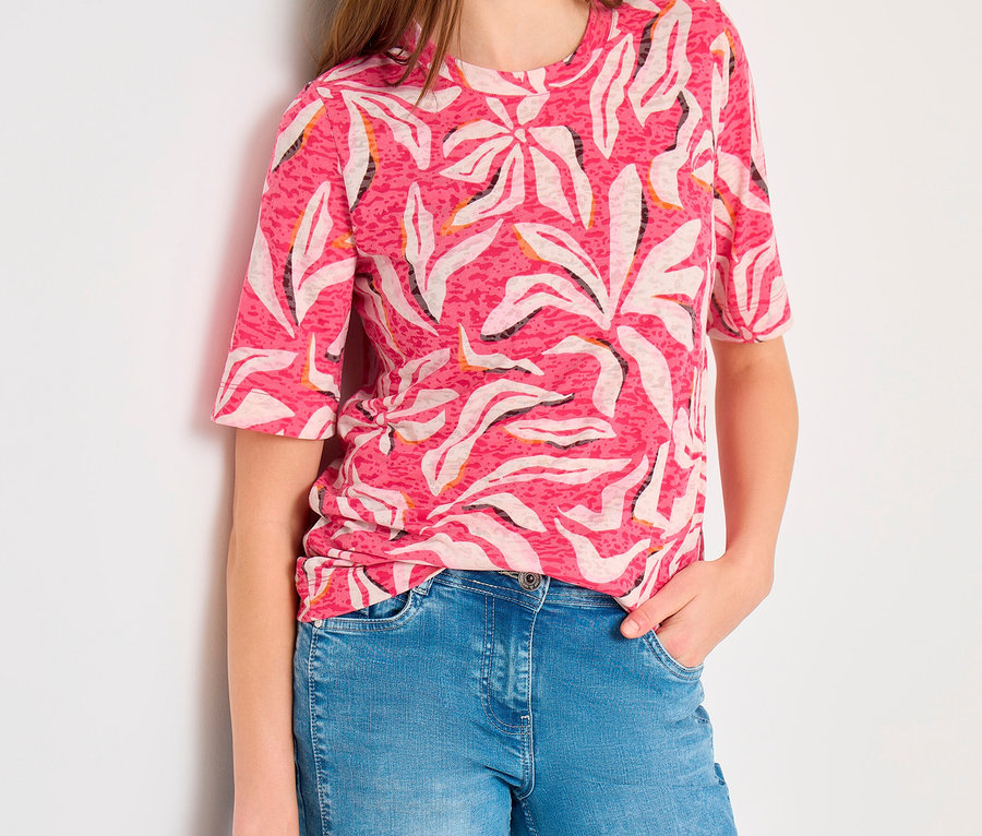 Frau trägt ein rosa CECIL Kurzarmshirt mit weißem und schwarzem abstraktem Muster, blaue Jeans und hält eine dunkelgraue Tasche.
