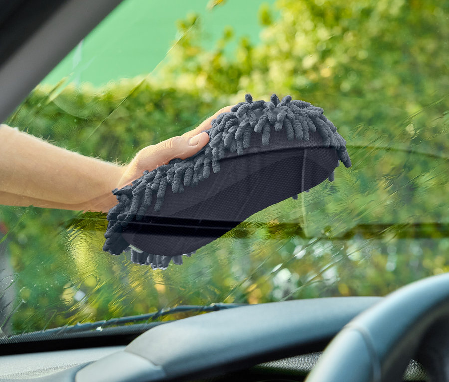 Eine Hand wischt mit einem grauen Waschlappen eine Autoscheibe.