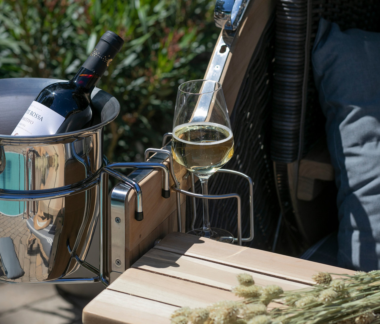 Eine Flasche Rotwein in einem silbernen Eiskübel neben einem Weinglas Weißwein auf einem Holztisch.