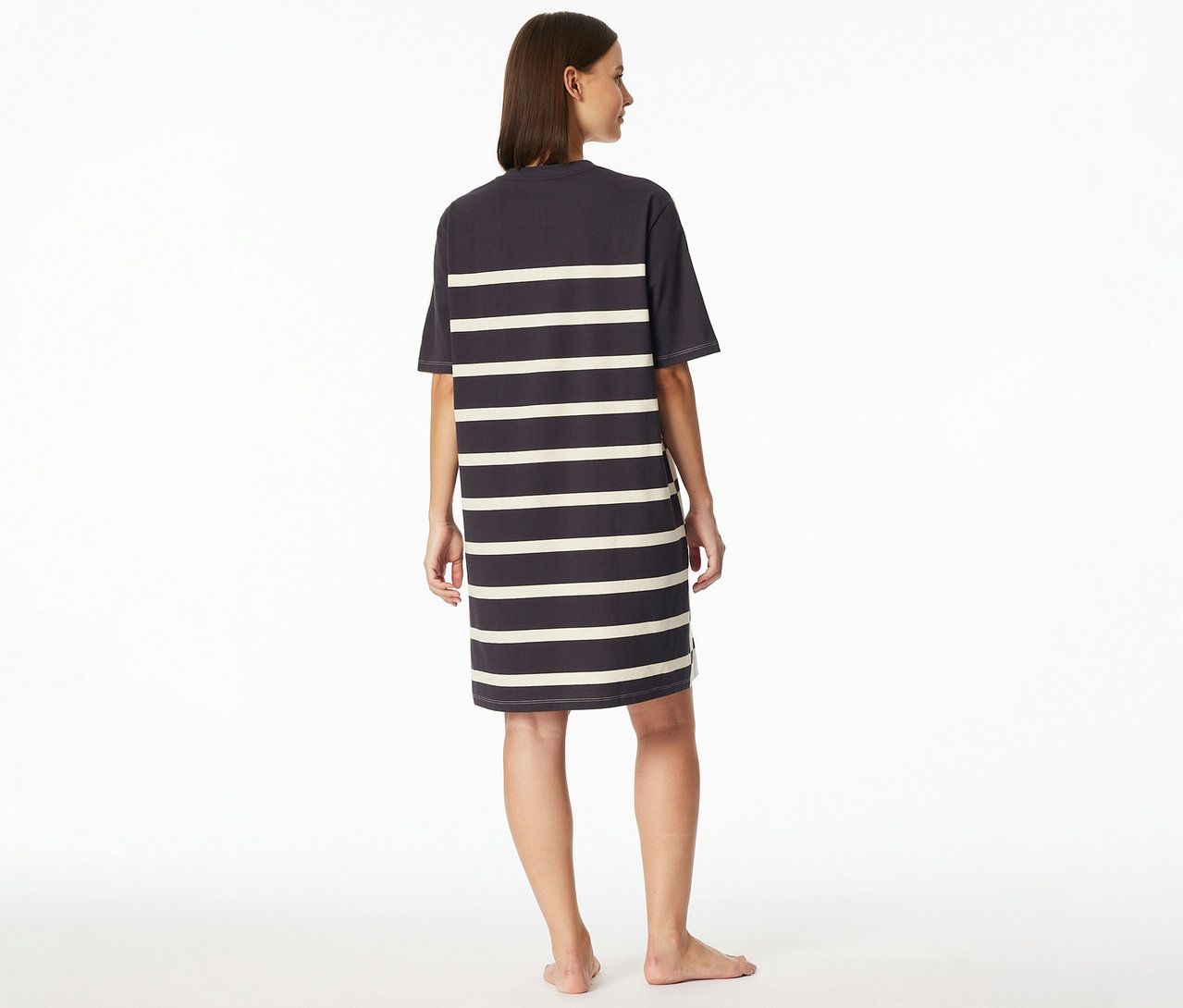Eine Frau steht barfuss mit dem Rücken zur Kamera, blickt leicht nach rechts und trägt ein gestreiftes SCHIESSER Nachthemd.