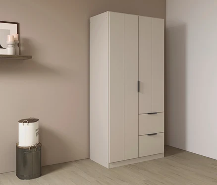 Beiger Kleiderschrank mit zwei Schubladen steht auf Holzboden. An der Wand hängen ein Regal und zwei dekorative Behälter.