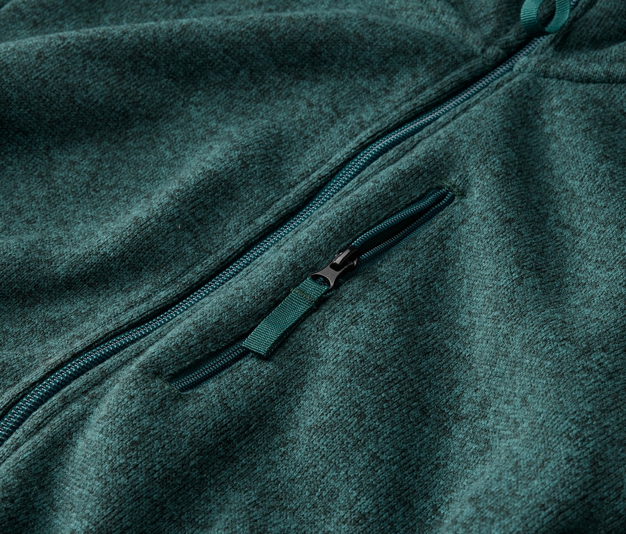 Nahaufnahme einer petrolfarbenen Fleecejacke mit durchgehendem Reißverschluss und Brusttasche mit Reißverschluss.