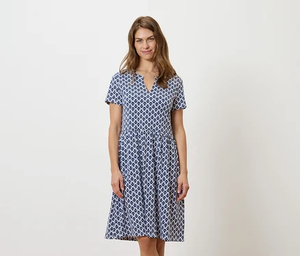 Frau steht und trägt ein blau-weißes Kleid.