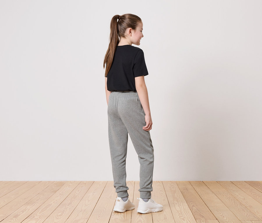 Mädchen mit Pferdeschwanz trägt ein schwarzes T-Shirt, graue Jogginghose und weiße Turnschuhe.