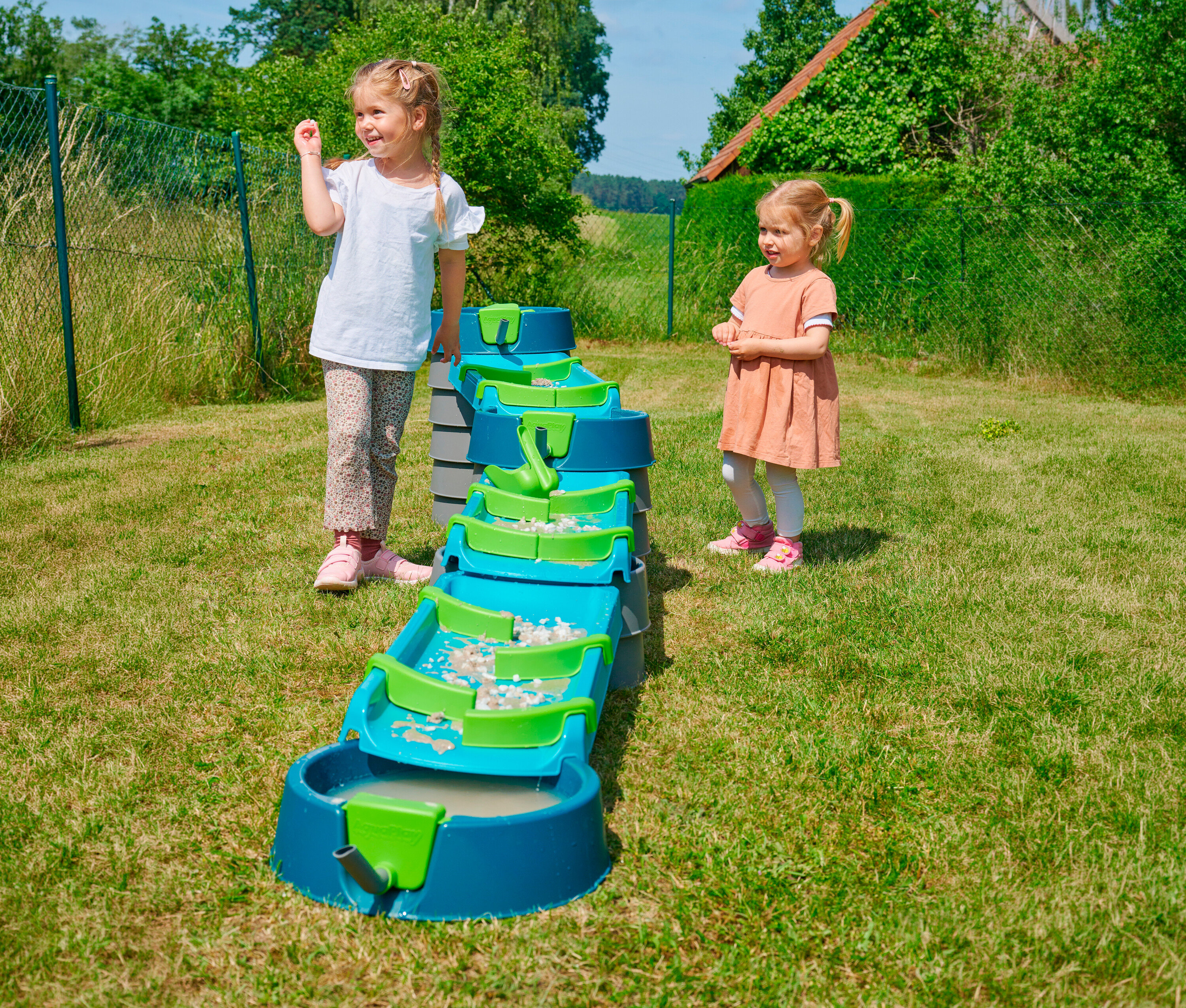 Zwei Mädchen spielen mit der AquaPlay »Mudway STREAM« Matschbahn im Garten.