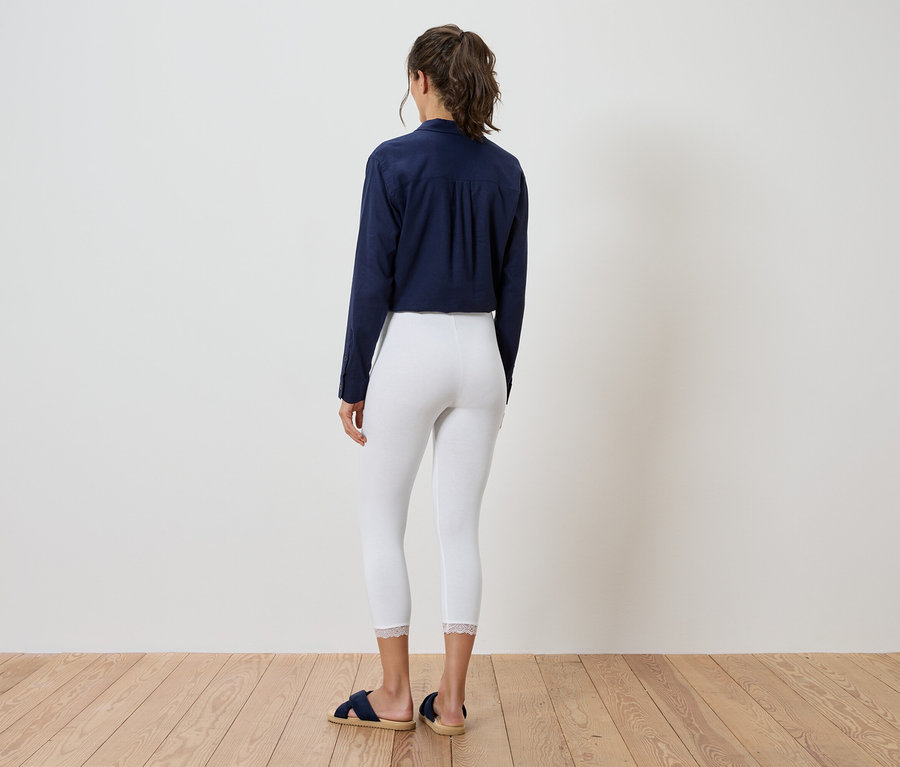 Eine Frau steht mit dem Rücken zur Kamera, trägt eine marineblaue Bluse, weiße Leggings und blaue Sandalen.