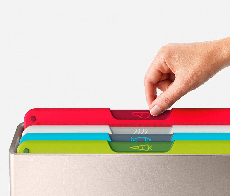 Eine Hand zieht ein rotes Schneidebrett aus einem Set von bunten Schneidebrettern in einem silbernen Behälter.