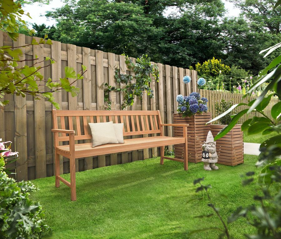 Eine Holzbank mit Kissen steht auf einem Rasen. Dahinter stehen zwei Pflanzsäulen »Tinus« mit blauen Blumen.