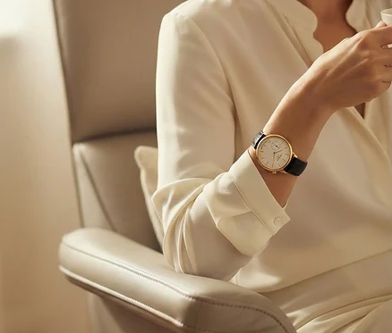 Frau mit goldener Armbanduhr und schwarzem Lederarmband sitzt in einem Sessel und hält eine Tasse.