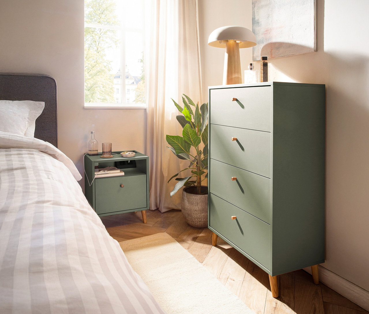 Schlafzimmer-Interieur mit pistazienfarbenem »Bjarne« Nachttisch mit Ladefunktion neben einem Bett und einer Kommode.