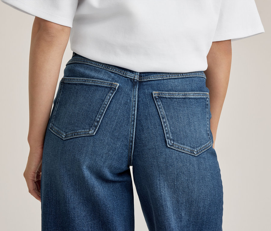 Rückenansicht einer Person in blauen Jeans mit zwei Gesäßtaschen und einem weißen T-Shirt.