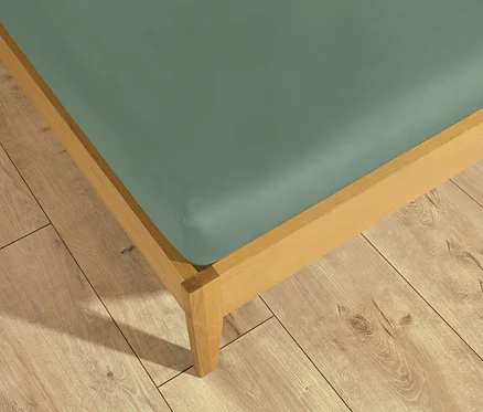 Ein Bett mit einem salbeigrünen SCHÖNER WOHNEN Spannbettlaken auf einem hellen Holzfußboden.