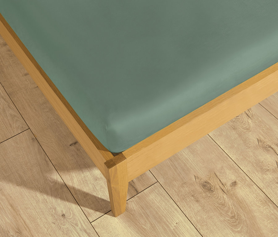 Ein Bett mit einem salbeigrünen SCHÖNER WOHNEN Spannbettlaken auf einem hellen Holzfußboden.