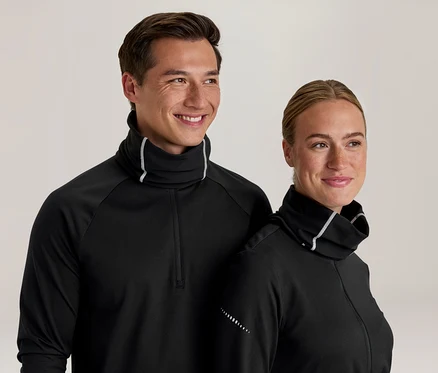 Lächelnder Mann und lächelnde Frau in schwarzen Langarmshirts mit hohem Kragen und weißem Besatz. Das Shirt des Mannes hat einen Viertelreißverschluss, beide haben reflektierende Punkte an den Ärmeln.