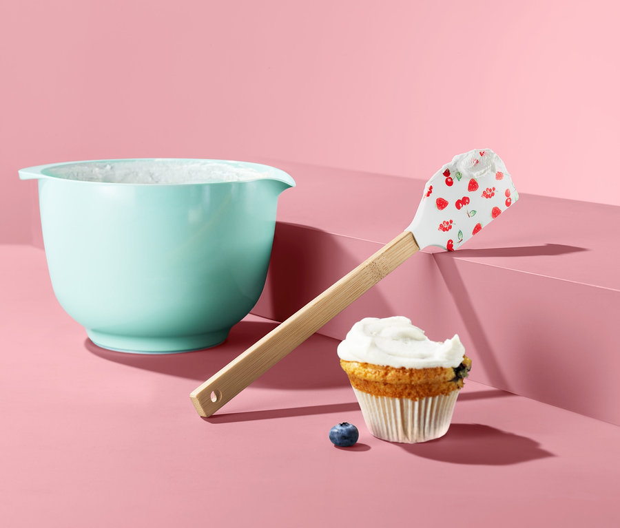 Hellblaue Schüssel neben einem Teigschaber, einem Muffin und einer Blaubeere.
