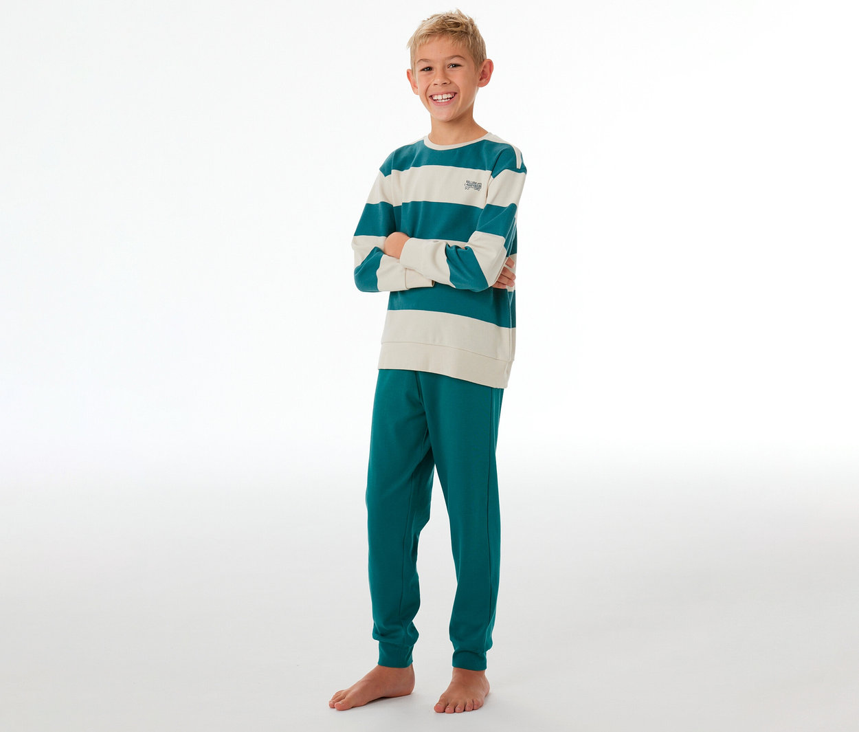 Ein lächelnder Junge steht mit verschränkten Armen und trägt einen SCHIESSER Kinder-Interlock-Pyjama. Das langärmlige Oberteil ist petrol-creme gestreift, die Hose petrolfarben.
