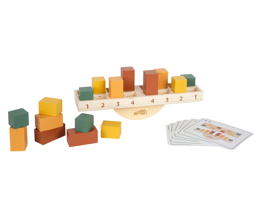 Ein Holz-Balancierspiel mit farbigen Bauklötzen in Grün, Gelb, Orange und Braun, die auf einer Wippe mit Zahlen von 1 bis 4 und daneben gestapelt sind, sowie ein Stapel Spielkarten mit Farbmustern.